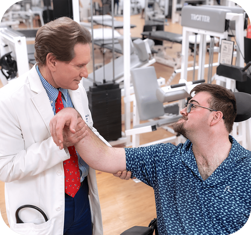 Dr. Craig H. Lichtblau in white coat examining a patient's arm during physical rehabilitation therapy.